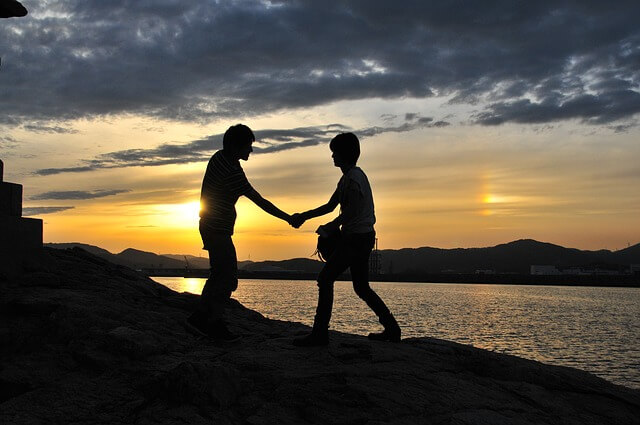 夕日の海辺で、二人の人物が、手をつなぐ画像